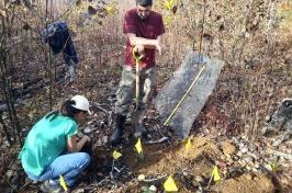 Two researchers (1 male standing, 拿着铲子, 1女蹲在旁边整)在规定的烧伤地点工作种植盆栽红橡树.